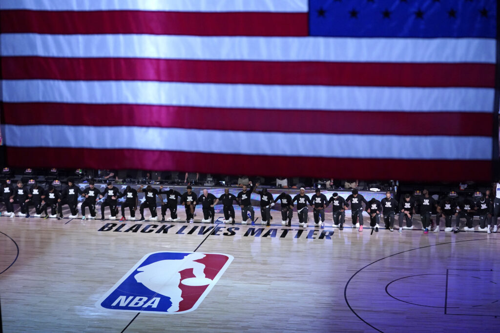 Members of the Orlando Magic and Brooklyn Nets kneel around a Black Lives Matter logo during the national anthem before the start of an NBA basketball game.