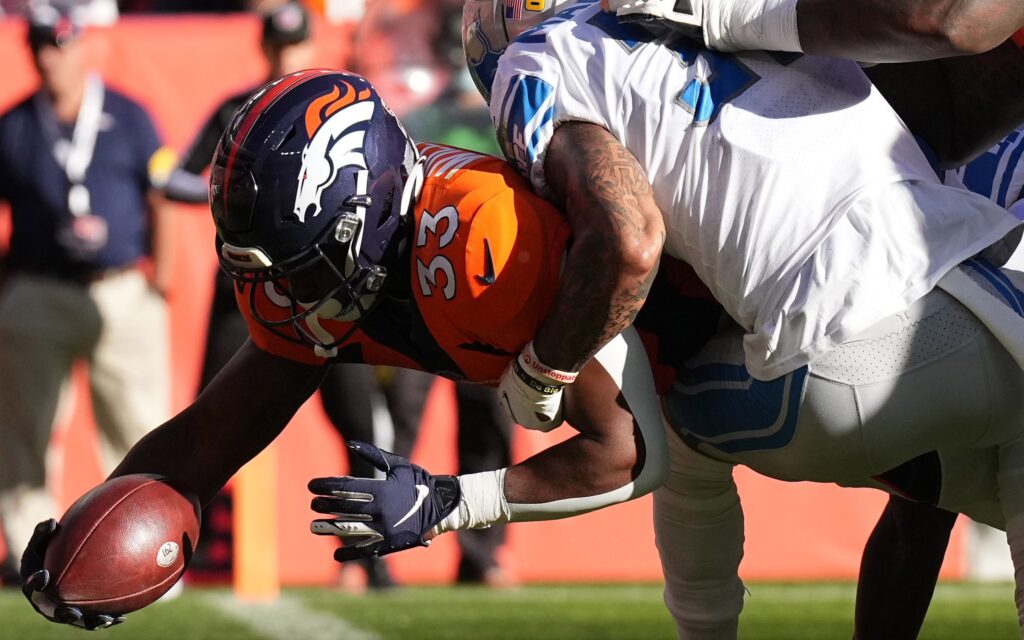 Javonte Williams dives over the goal line through two defenders. Credit: Ron Chenoy, USA TODAY Sports.