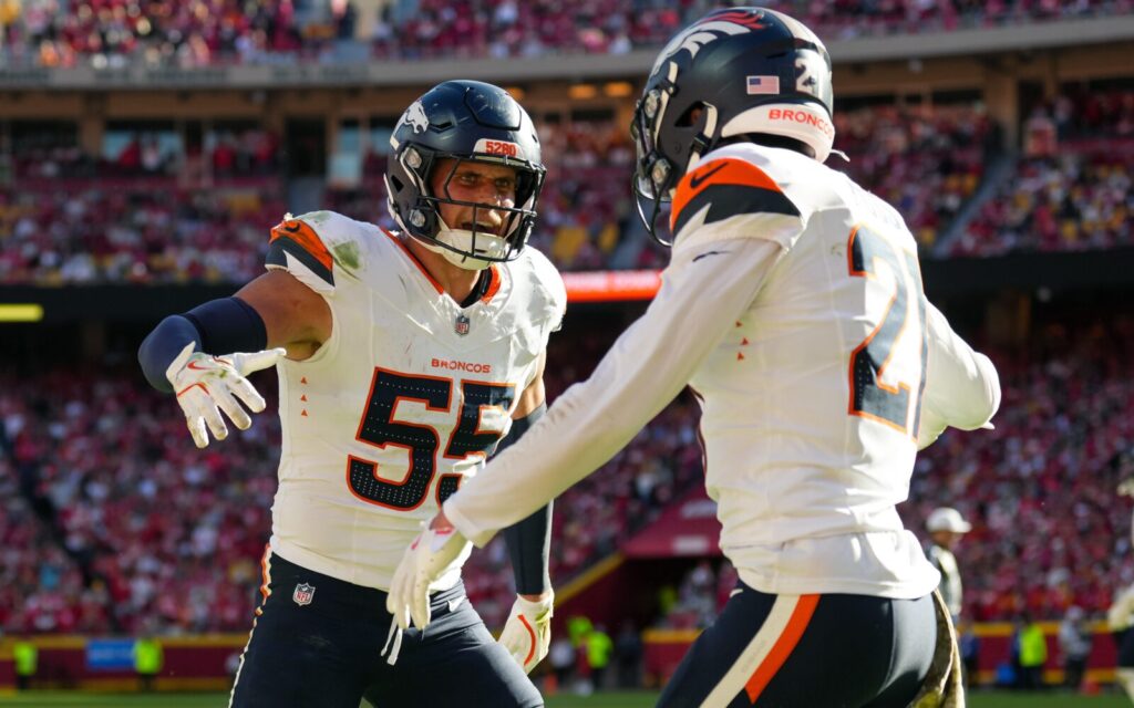 Broncos players Cody Barton and Riley Moss celebrate a successful play in Kansas City by standing and starting a high five, while Barton smiles at Moss.