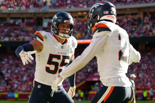 Broncos players Cody Barton and Riley Moss celebrate a successful play in Kansas City by standing and starting a high five, while Barton smiles at Moss.