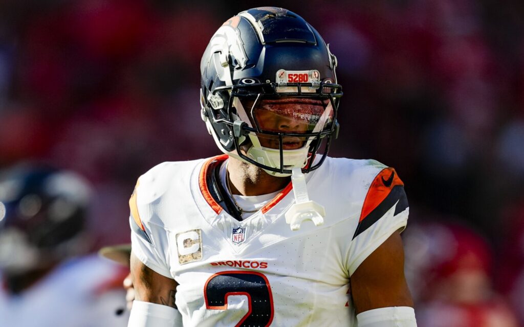 Patrick Surtain stares during a game. He's wearing the Broncos white away jersey and the 2024 helmet which is matte blue.