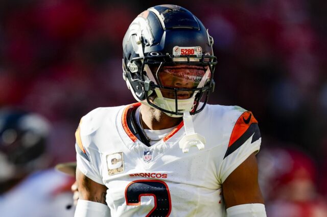 Patrick Surtain stares during a game. He's wearing the Broncos white away jersey and the 2024 helmet which is matte blue.