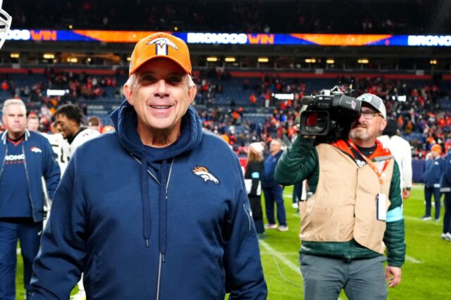 Sean Payton smiles onfield after the Broncos - Browns game on Monday Night. He's followed by a camera man and other personnel.