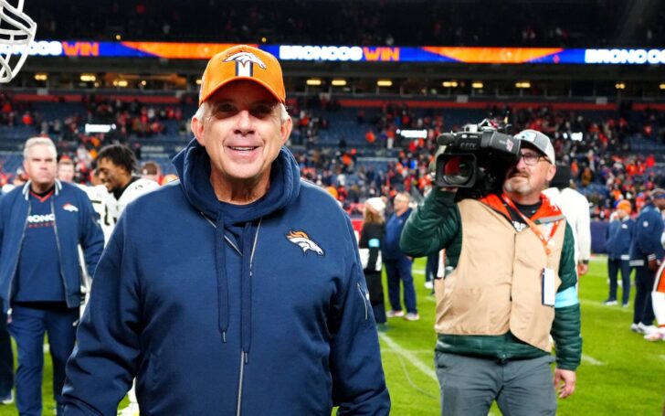 Sean Payton smiles onfield after the Broncos - Browns game on Monday Night. He's followed by a camera man and other personnel.