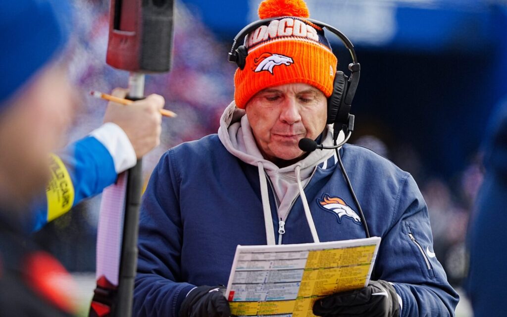 Sean Payton calling plays against the Bills. He has on an orange Broncos beanie, blue Broncos zip-up over a grey hoodie.