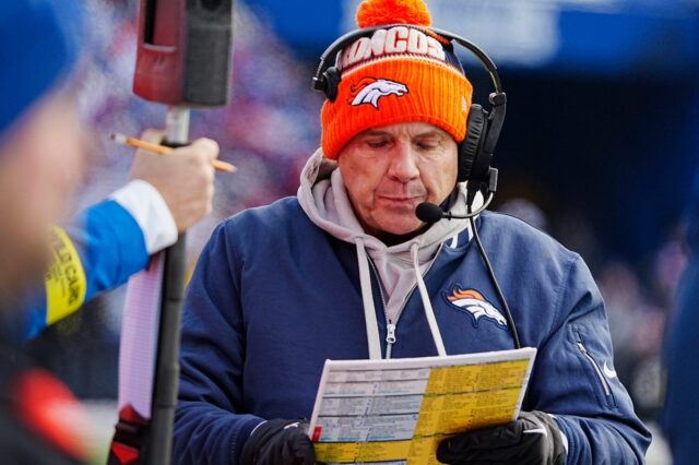 Sean Payton calling plays against the Bills. He has on an orange Broncos beanie, blue Broncos zip-up over a grey hoodie.