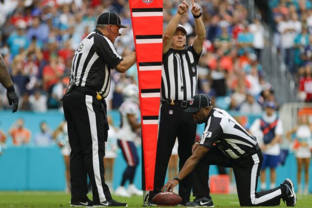 A referee signals the ball is short by inches. Another officer holds the chain while a third official holds the ball.