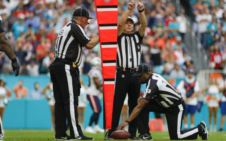 A referee signals the ball is short by inches. Another officer holds the chain while a third official holds the ball.